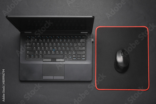 Black Laptop and PC mouse with PC mouse pad on a black background. Top view