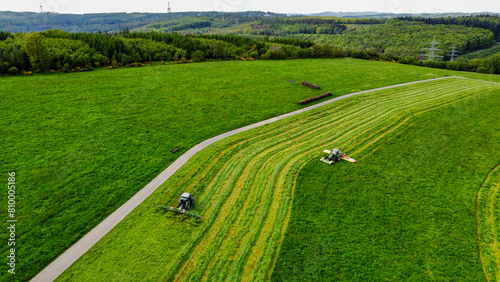 Landwirte mähen eine Wiese und wenden das Gras (Luftaufnahme)