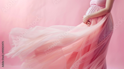 Close up of pregnant woman in a pink dress holding her belly on a pastel background,