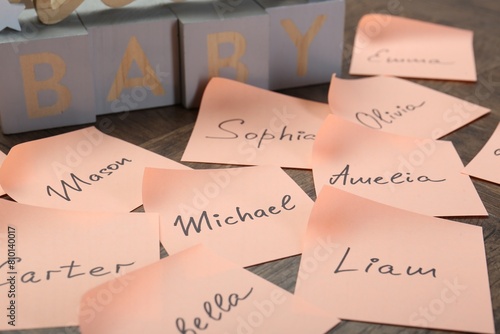 Paper stickers with different names on wooden table, closeup. Choosing baby's name