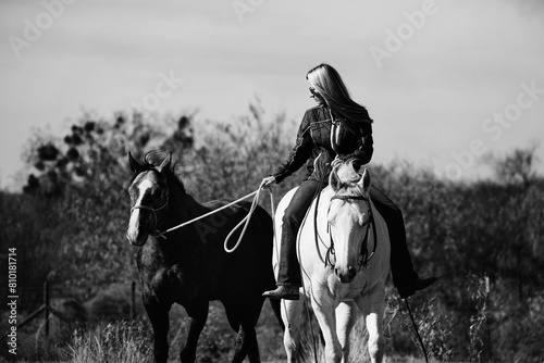 Woman riding horse bareback while ponying outdoors on ranch in black and white for western lifestyle.