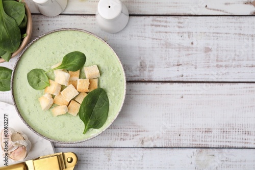 Delicious spinach cream soup with leaves and croutons in bowl on white wooden table, flat lay. Space for text