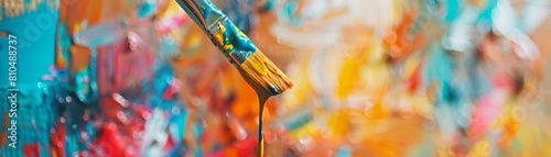 A closeup photo of a paintbrush dripping with vibrant paint, with a blurred artists studio full of colorful canvases in the background