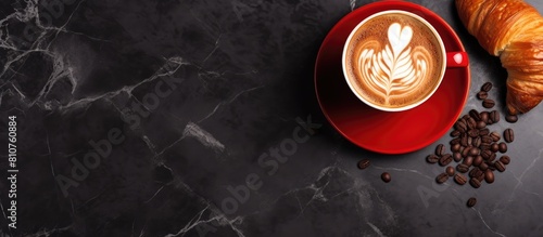 A top view of a cappuccino or latte in a red cup alongside a chocolate croissant on a dark marble background Perfect for breakfast with copy space for text