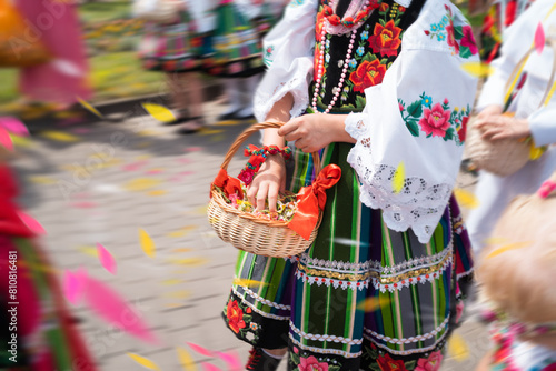 Girls in traditional Polish regional costumes throw flower petals during Łowicz Corpus Christi procession. Motion blur, movement