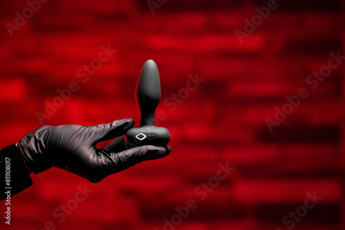 Silicone anal plug in a female hand in black latex gloves on a black background. Massager with multiple speeds. Sex shop products, adult gifts for couples.