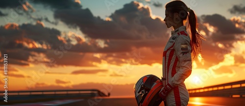 A woman racer in a racing suit holds a helmet against a vibrant sunset at a racetrack, embodying determination and readiness 5.