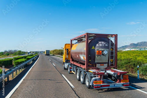 Truck driving on a highway with a tank container with labels and danger panels for toxic liquids according to the international treaty on dangerous goods. A.D.R.