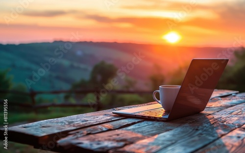 Sunset over a scenic view with a coffee cup and laptop on a wooden table.