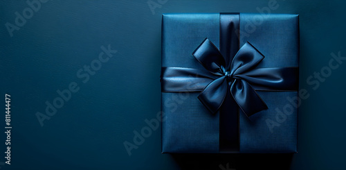 Dark blue gift box with ribbon and bow for man and boy isolated on blue background. Holiday gift with birthday or Christmas present. Copy space available for Father's Day celebration.