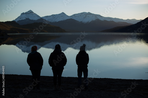 Three silhouette women looking at the reflection of snow capped mountains at a lagoon after sunset in patagonia during a clear winter day. Sofia lagoon, Puerto natales, Chile