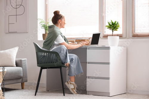 Young woman sitting at workplace and working with laptop in living room