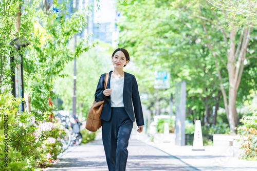 新緑の中を歩くスーツを着た女性