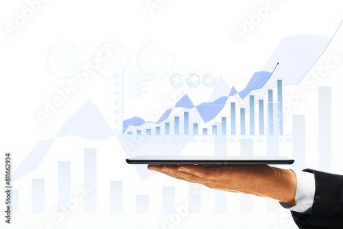 A person's hand holding a tablet with a digital graph, overlaid on a white background with financial symbols, symbolizing business growth