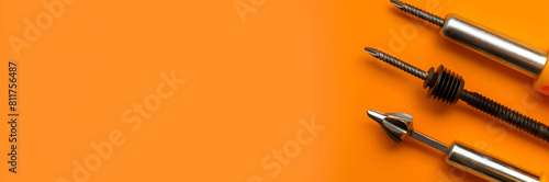 Screwdriver and screws web banner. Close-up of screwdriver and screws isolated on orange background with copy space.