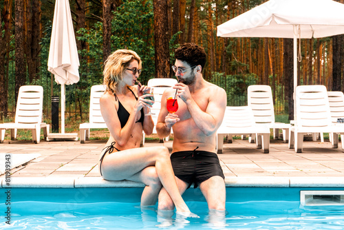 Romantic couple in sunglasses drinking their refreshing beverages at the poolside in the recreation area. Rest and relaxation concept