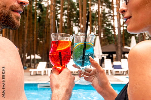 Romantic couple of tourists relaxing with refreshing drinks at the outdoor swimming pool at the holiday resort. Rest and relaxation concept