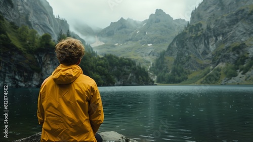 Man in yellow jacket seated mountain lake Swiss Alps contemplating misty landscape