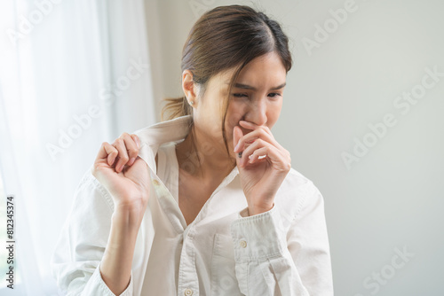 Bad smell nose concept asian young housewife woman having smelling clothes her shirt collar, sniff smelly dirty stinky musty, look disgusting from clothes after washed, laundry out of machine at home.