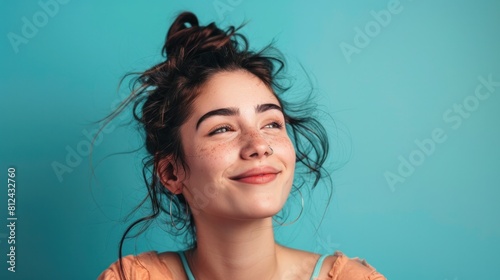 Woman with a septum ring looking away with a smile on her face. Carefree young woman standing alone against a turquoise background.