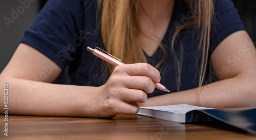 Dziewczyna trzyma w ręce różowy długopis i notuje listę zakupów 