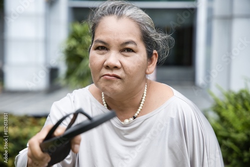 Angry old senior woman holding slipper and being ready to slap or hurt you, concept image of violence, aggression, physical assault, anger management