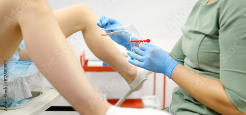 Gynecologist examines a patient laying on gynecological chair using medical vaginal speculum. Doctor takes a smear from a young woman cervix. Diagnosis of diseases.