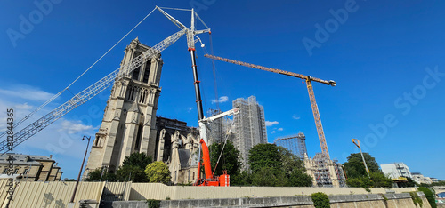 Restoration of Notre-Dame Cathedral, Paris, after major fire damage, with scaffolding, cranes and barriers; repairs of famous French cathedral Notre Dame in Paris under a clear blue sky.