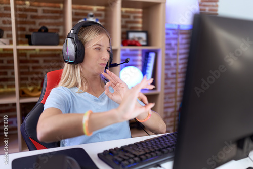 Young caucasian woman playing video games wearing headphones disgusted expression, displeased and fearful doing disgust face because aversion reaction.