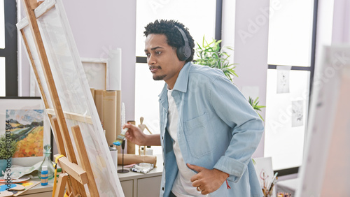 Handsome man with headphones painting on an easel in a bright studio