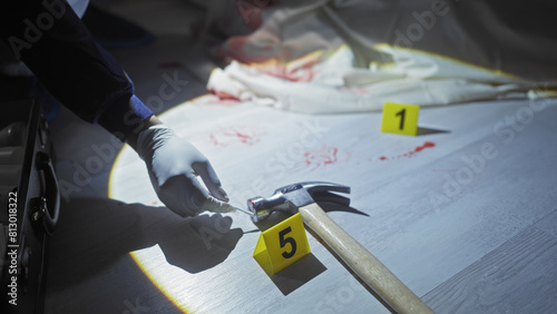 A forensic investigator examines a bloodied hammer at a crime scene with evidence markers in a dimly lit room.