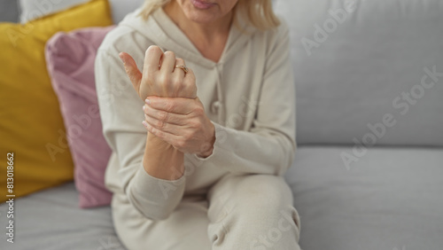 A caucasian woman experiencing wrist pain at home, sitting on a sofa with colorful pillows in a cozy living room setting.