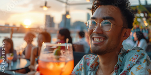 Close-up on a man admiring city skyline at having a drink at a busy rooftop bar on a summers evening