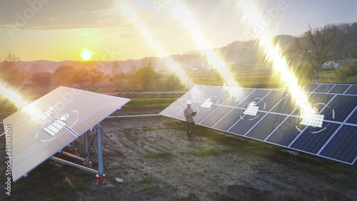 Solar panels farm at sunset, engineer technician working on site with smart tablet device checking the inclination angle of the sun ray