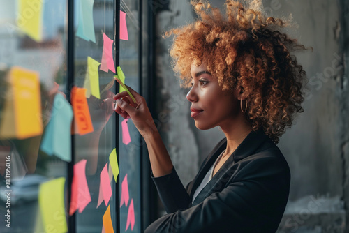 Photo of a female businesswoman using sticky notes on glass office wall