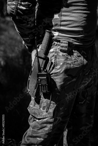 A military knife and a walkie-talkie hang on the belt of a soldier in uniform. Military equipment, tactical equipment, equipment for combat operations. Black and white photo