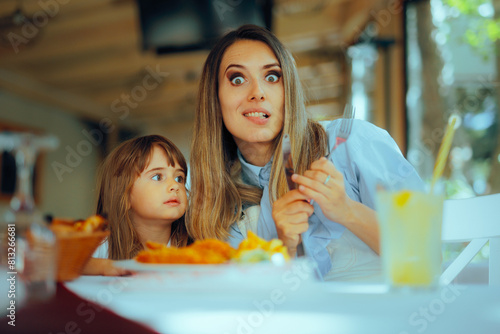 Cheerful Mother Eating Lunch with her Toddler Daughter. Happy family sitting in a restaurant waiting the dish to cool off 