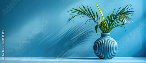 Minimalist blue background with a palm leaf in cobalt vase, simple composition with lots of space