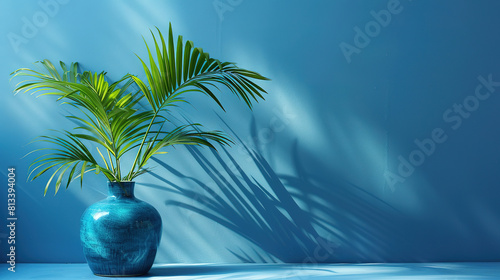 Minimalist blue background with a palm leaf in cobalt vase, simple composition with lots of space