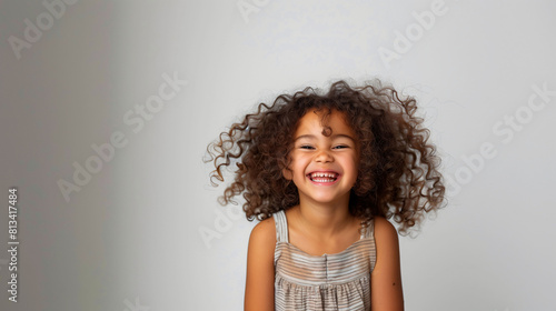 Six-year-old girl with curly hair laughing, carefree expression, casual outfit, bright background, joyful, innocent moment. 