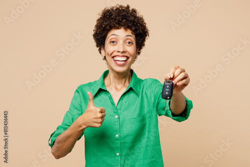 Young woman of African American ethnicity in green shirt casual clothes hold in hand car key fob keyless system show thumb up isolated on plain pastel light beige background studio Lifestyle concept