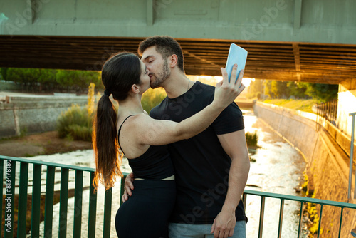 Pareja haciéndose un selfie con el móvil. Enamorados en el rio. Pareja deportista haciendose una foto en el parque. Estilo de vida. Beso de novios