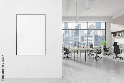 A modern office interior with a blank poster on the wall, large windows overlooking Bangkok cityscape, and a workspace setup, 3D Rendering