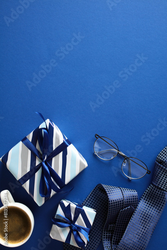 Gift Set on Blue. Top view of a neat gift arrangement with two wrapped presents, eyeglasses, a coffee cup, and a rolled tie on a elegant blue background. Ideal for gifting and celebration themes.