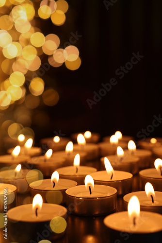 Many burning candles in darkness, bokeh effect