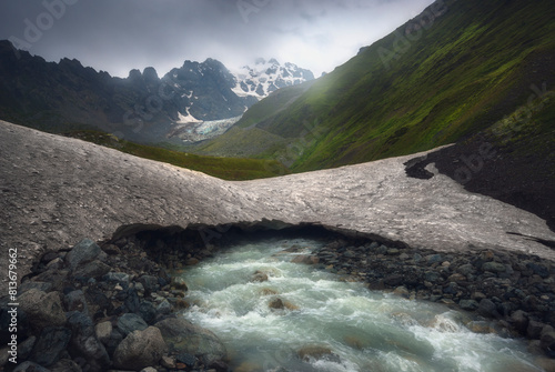 Fast mountain river flows under old glacier after rain