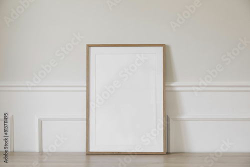 Minimal empty vertical wooden picture frame mockup. White wall with elegant stucco decor. Portrait large poster a3, a2 mock-up. Wooden table. Modern, minimal design. Scandinavian indoor interior.