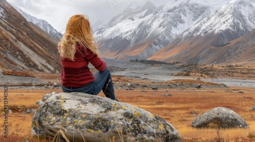Woman sitting on a rock, gazing at a mountainous landscape in Canterbury, New Zealand.