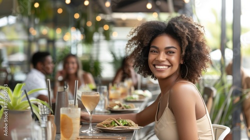 A joyful young woman laughs while eating at a restaurant, a plate of food and drinks in front of her.