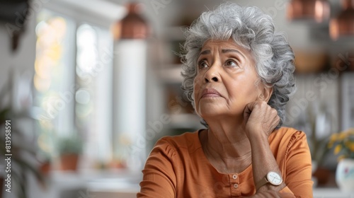 A senior biracial woman appears contemplative, sitting inside a home with a thoughtful expression.